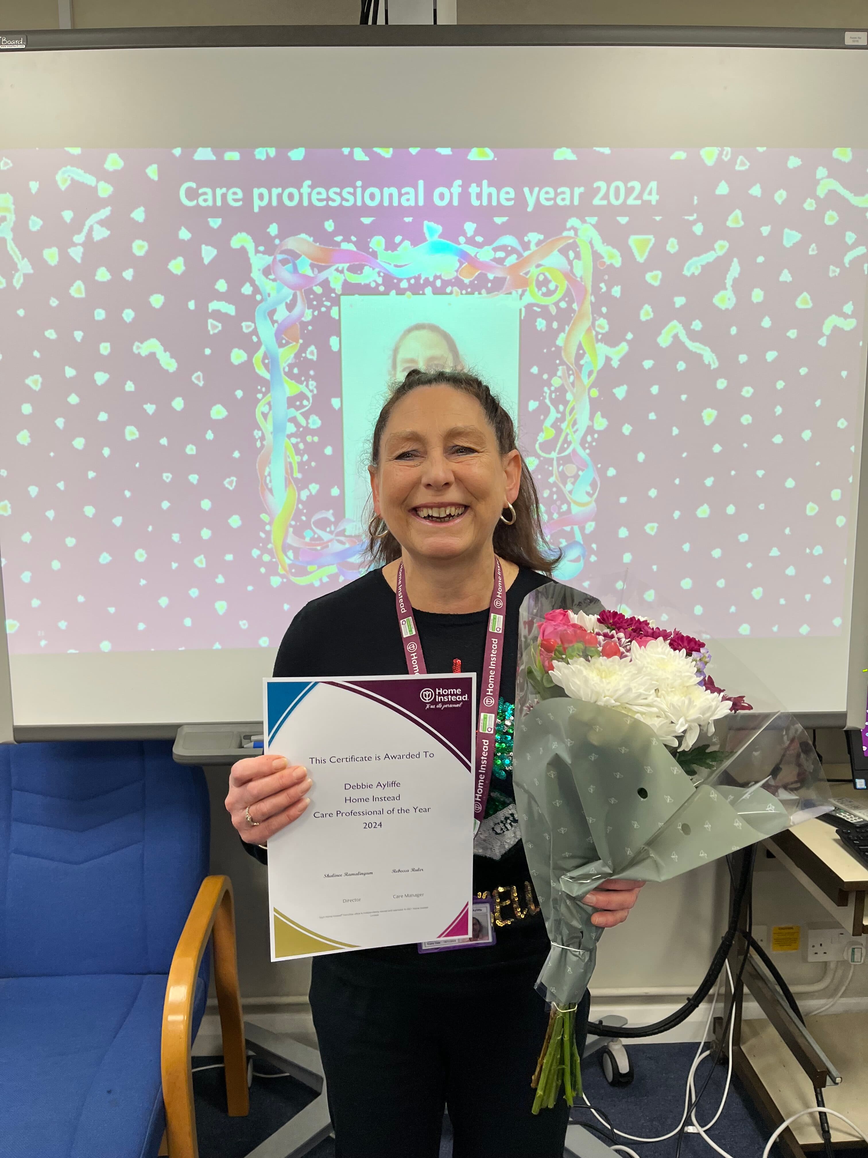 Care pro smiling with a certificate celebrating her care pro of the year award and also a bunch of flowers.