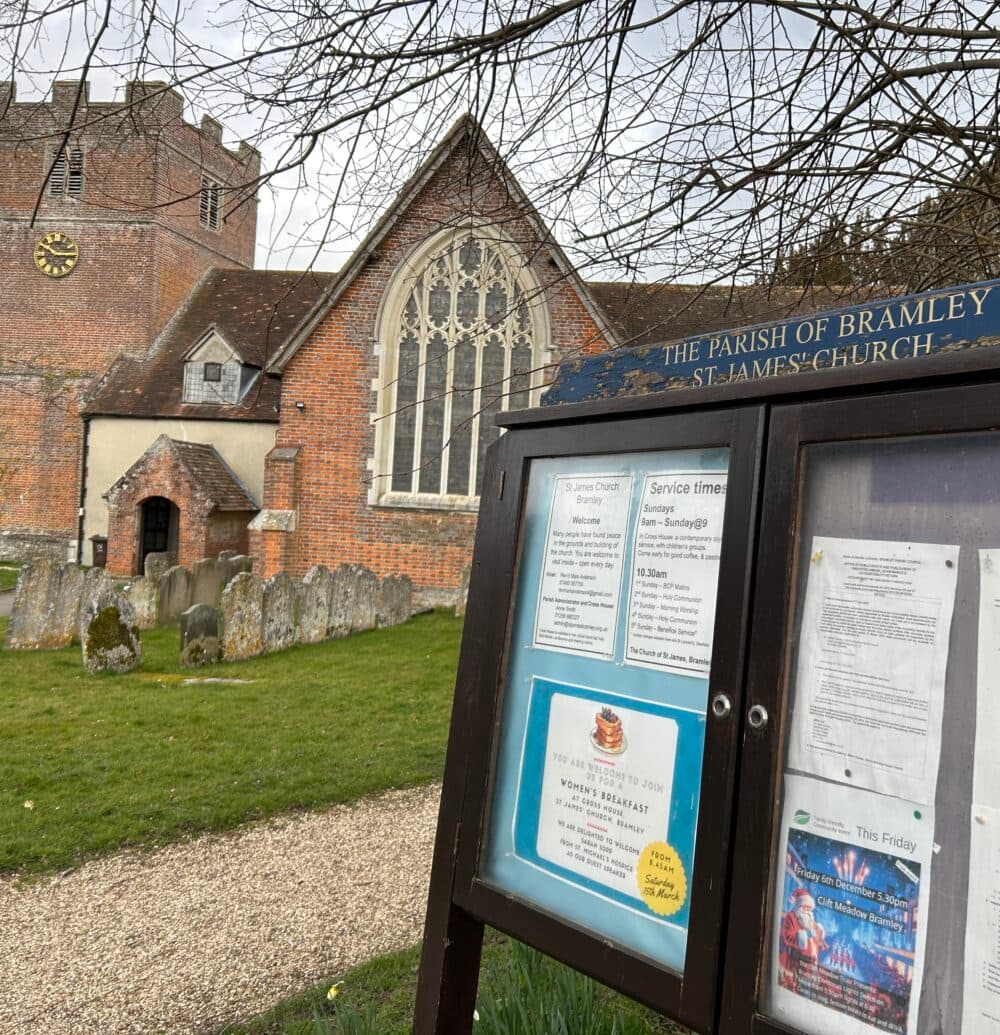 St James church in Bramley, showing a notice board alongside a gravel path through the graveyards and the entrance to the church