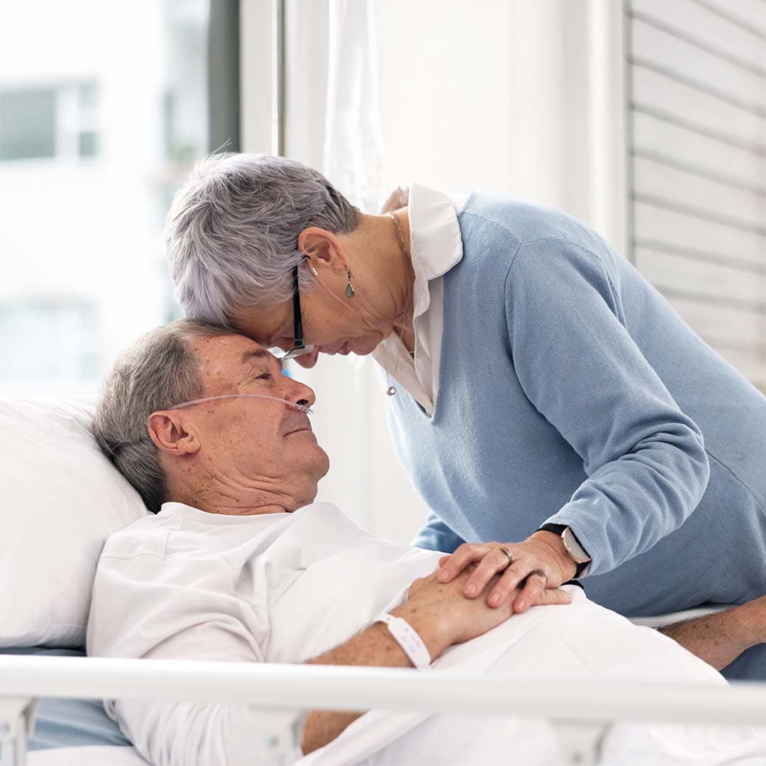 Elderly lady comforting her husband in a hospital bed