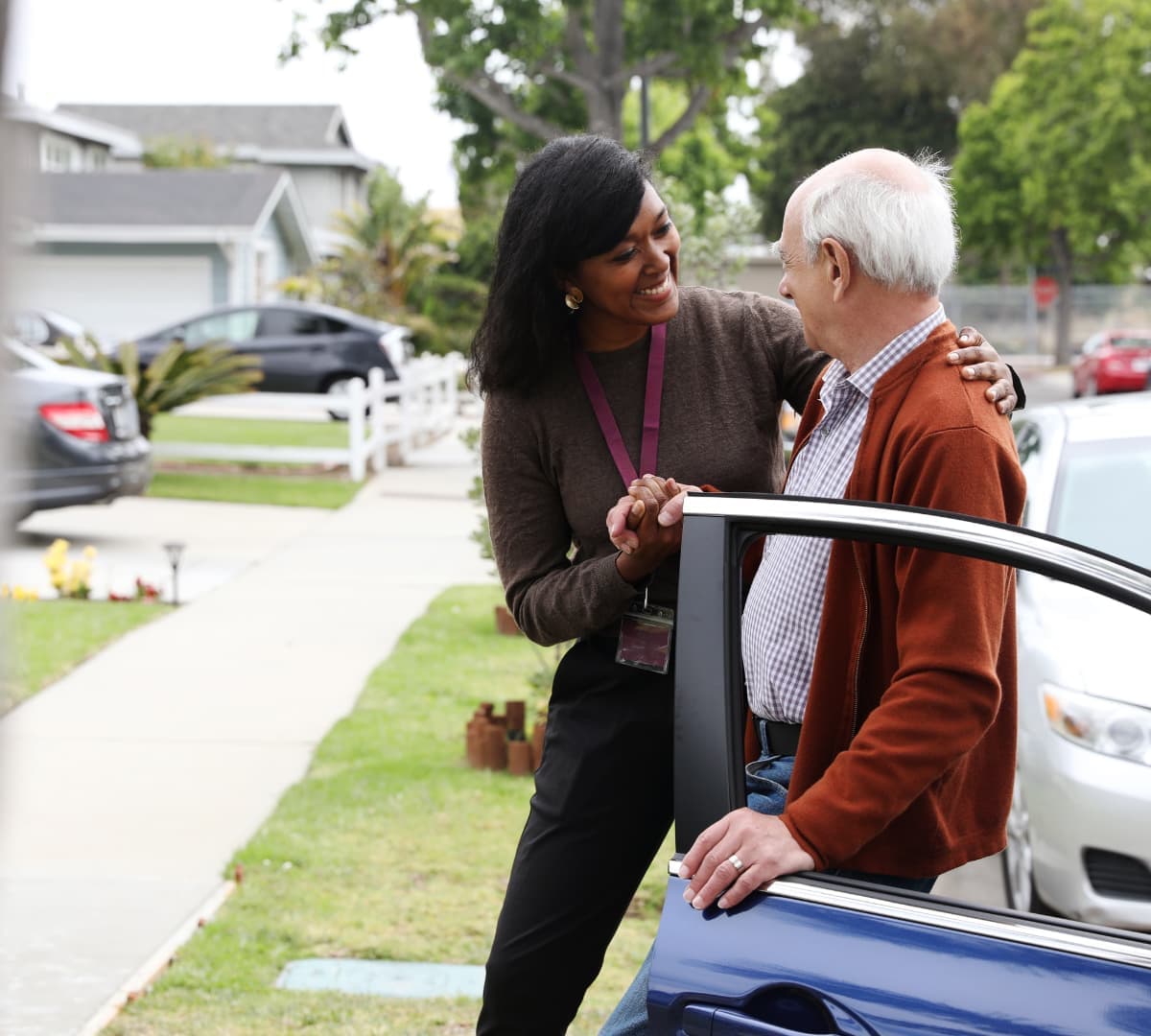 Older man with grey hair and with his younger female carer with black hair going out of the car