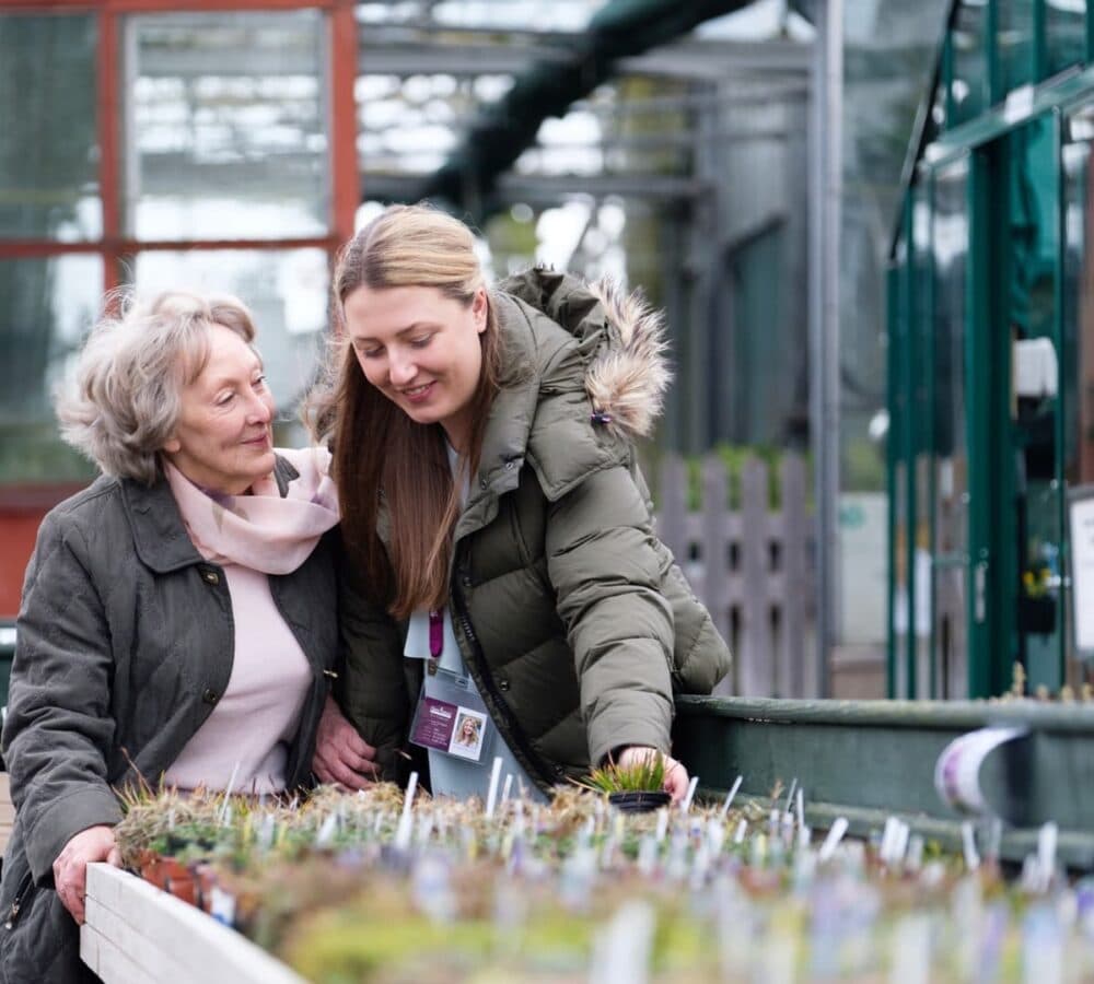 Older woman and her carer both happy and smiling while wearing winter clothes out in the garden store