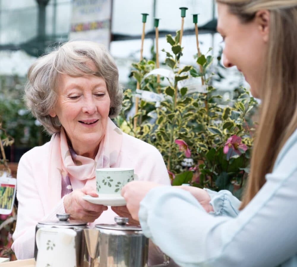 Older woman with short grey hair having a cup of tea with her carer outdoors