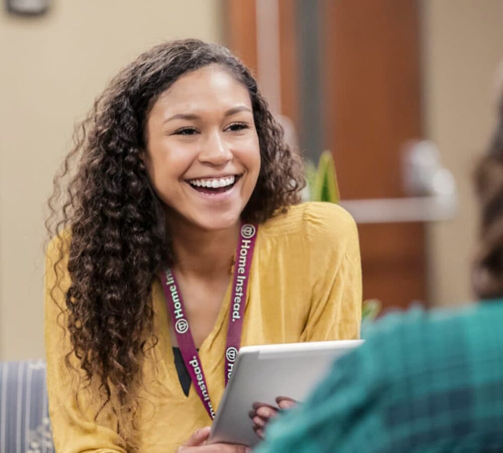 Woman with long curly hair and wearing yellow top smiling and happy inside the office