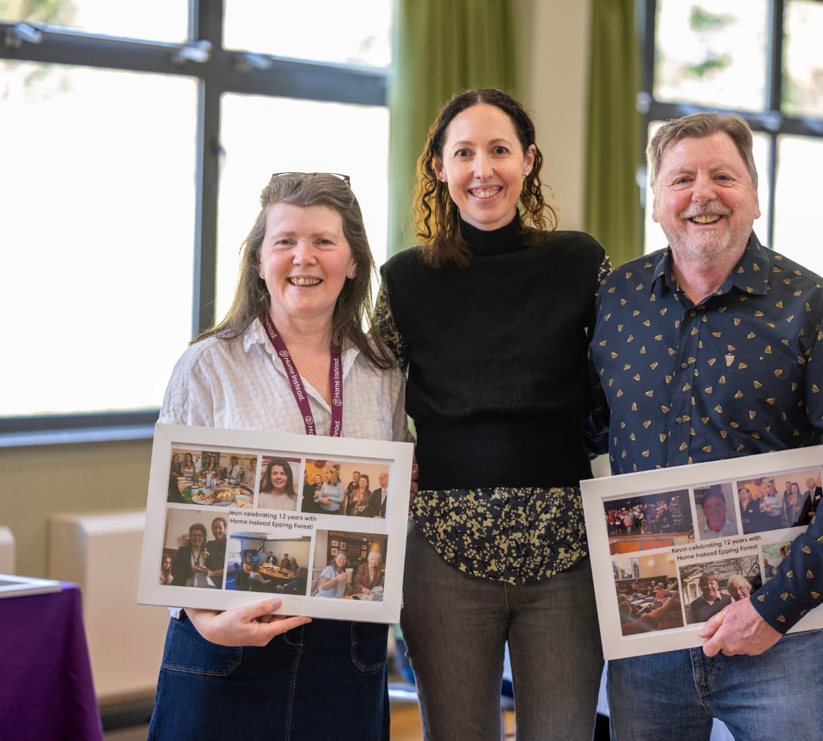 Three people standing and smiling while holding photos
