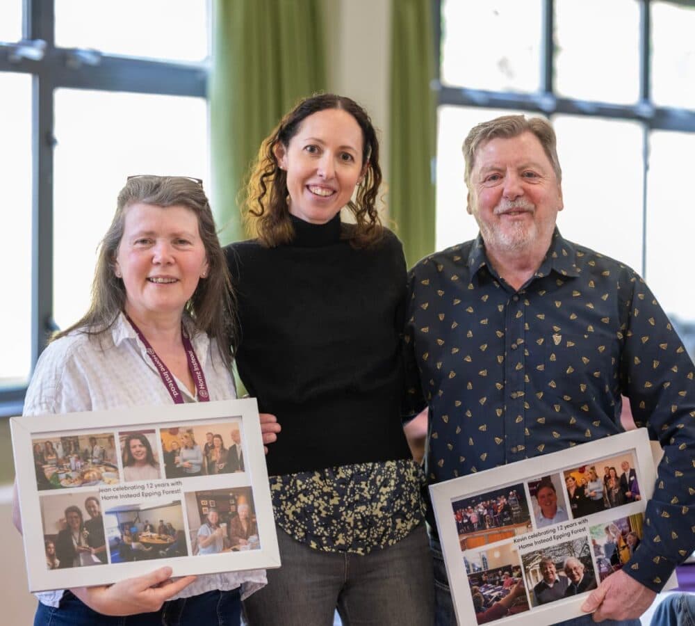 Three people smile indoors, holding framed photo collages with memories and messages. - Home Instead