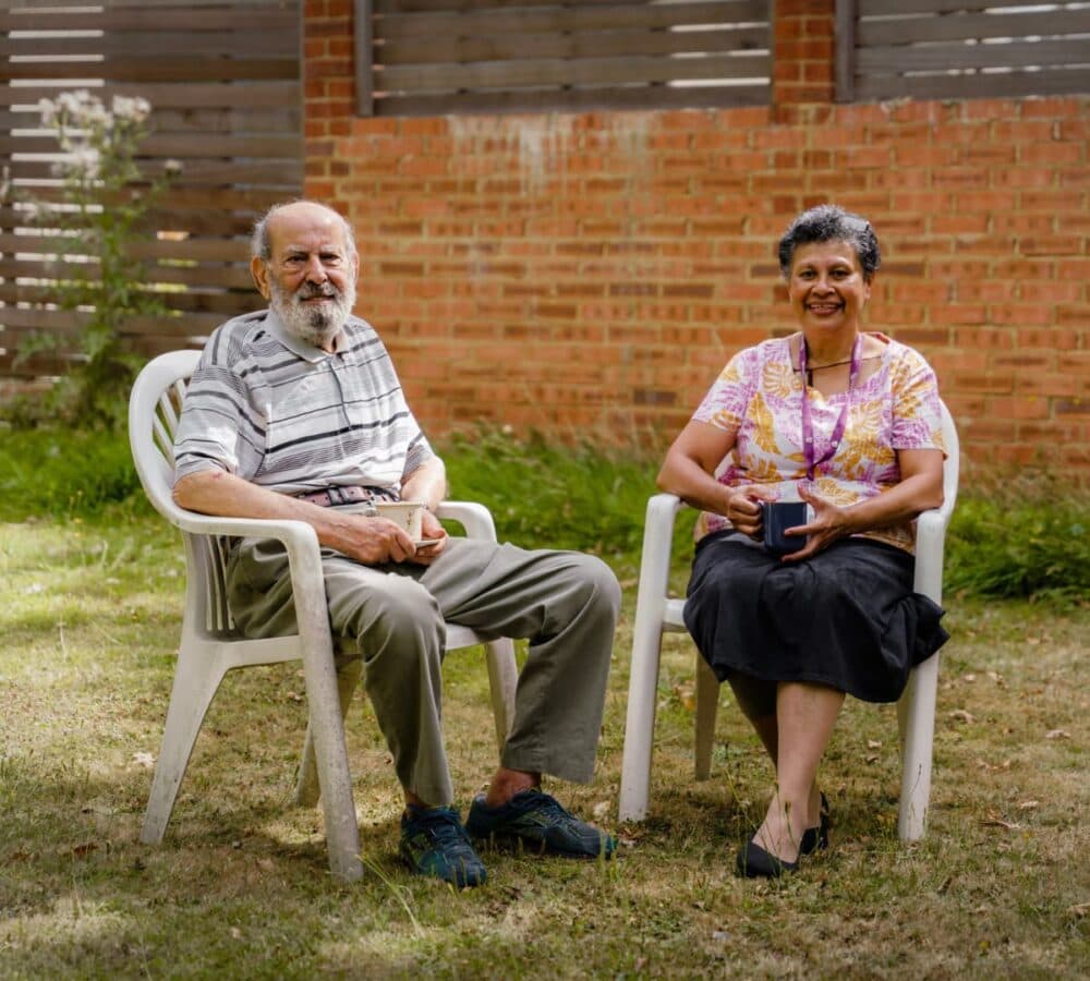 An older man sitting outdoors with his younger female carer surrounded by green grass