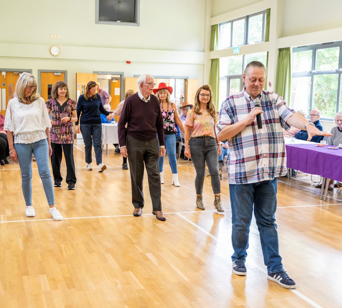 Group of people happily dancing inside the hall while the male leader is holding a mic