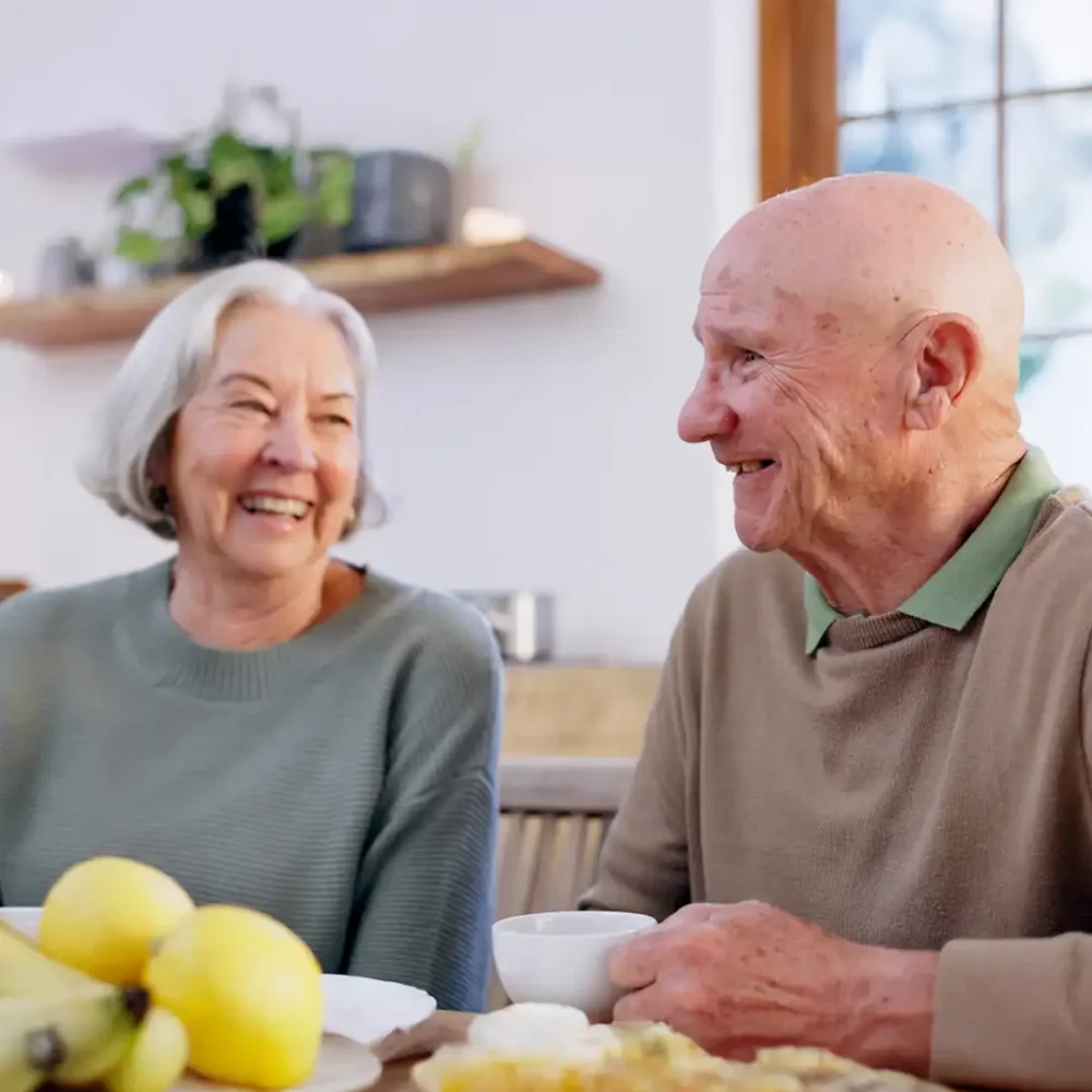 Senior couple sitting together at home laughing and enjoying a cup of tea
