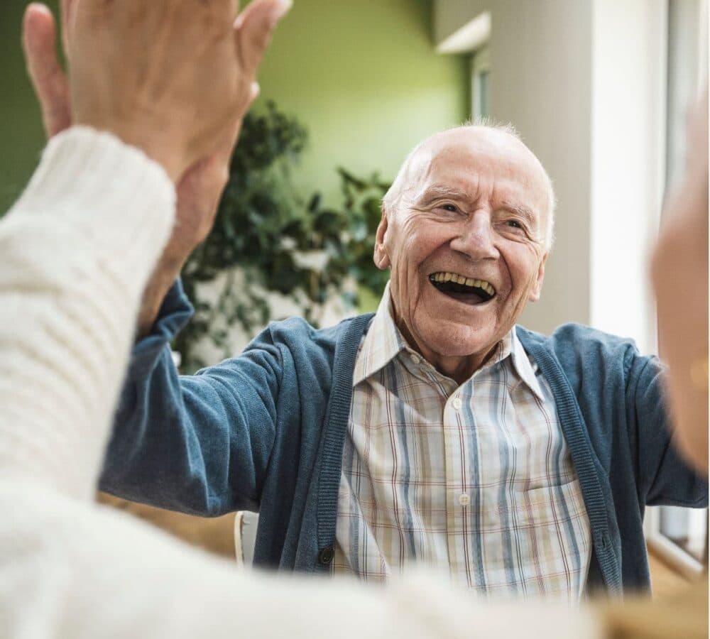 A happy older male adult with white hair raising his hands while smiling and being happy