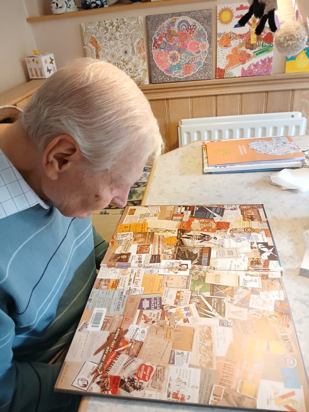 An elderly man looks closely at a colorful jigsaw puzzle on a table in a cozy room. - Home Instead