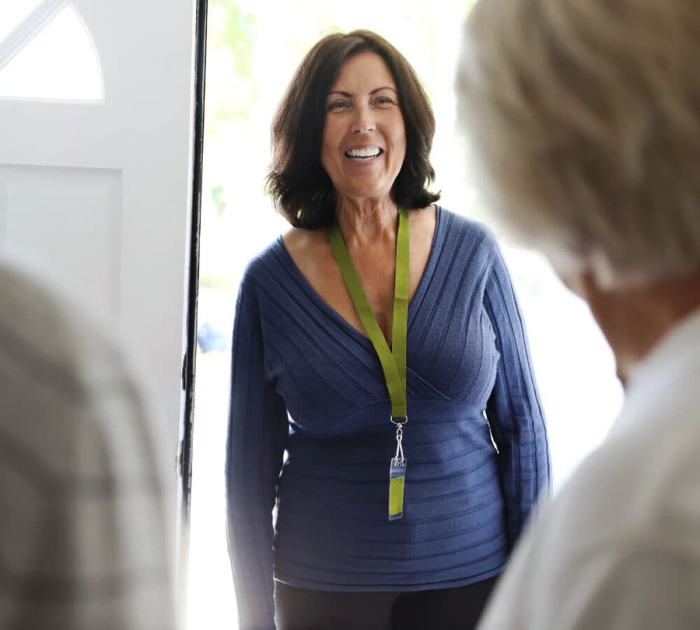 A woman at the door with black hair and wearing blue top happy and smiling at the door