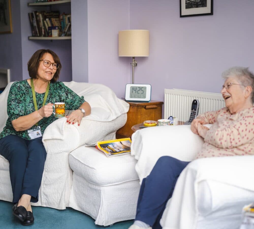 Two women sitting on a white couch while chatting and drinking coffee