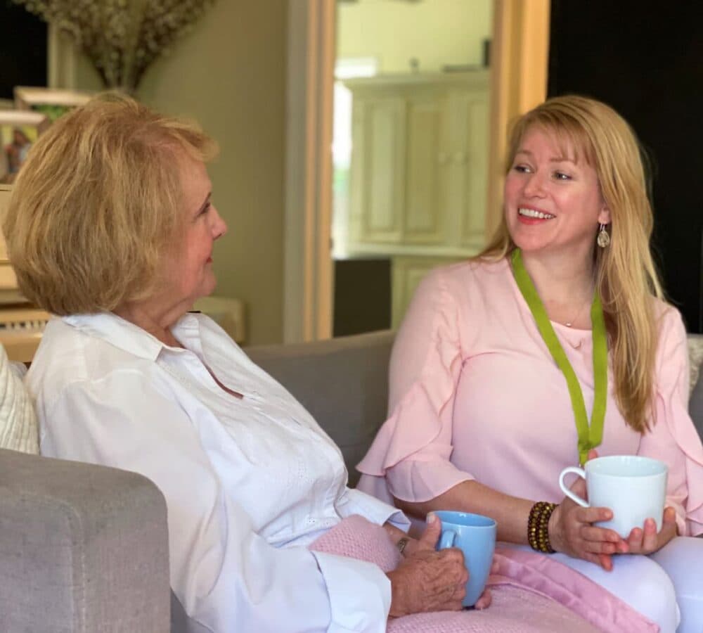 Two women sitting on a couch while having coffee and chatting together