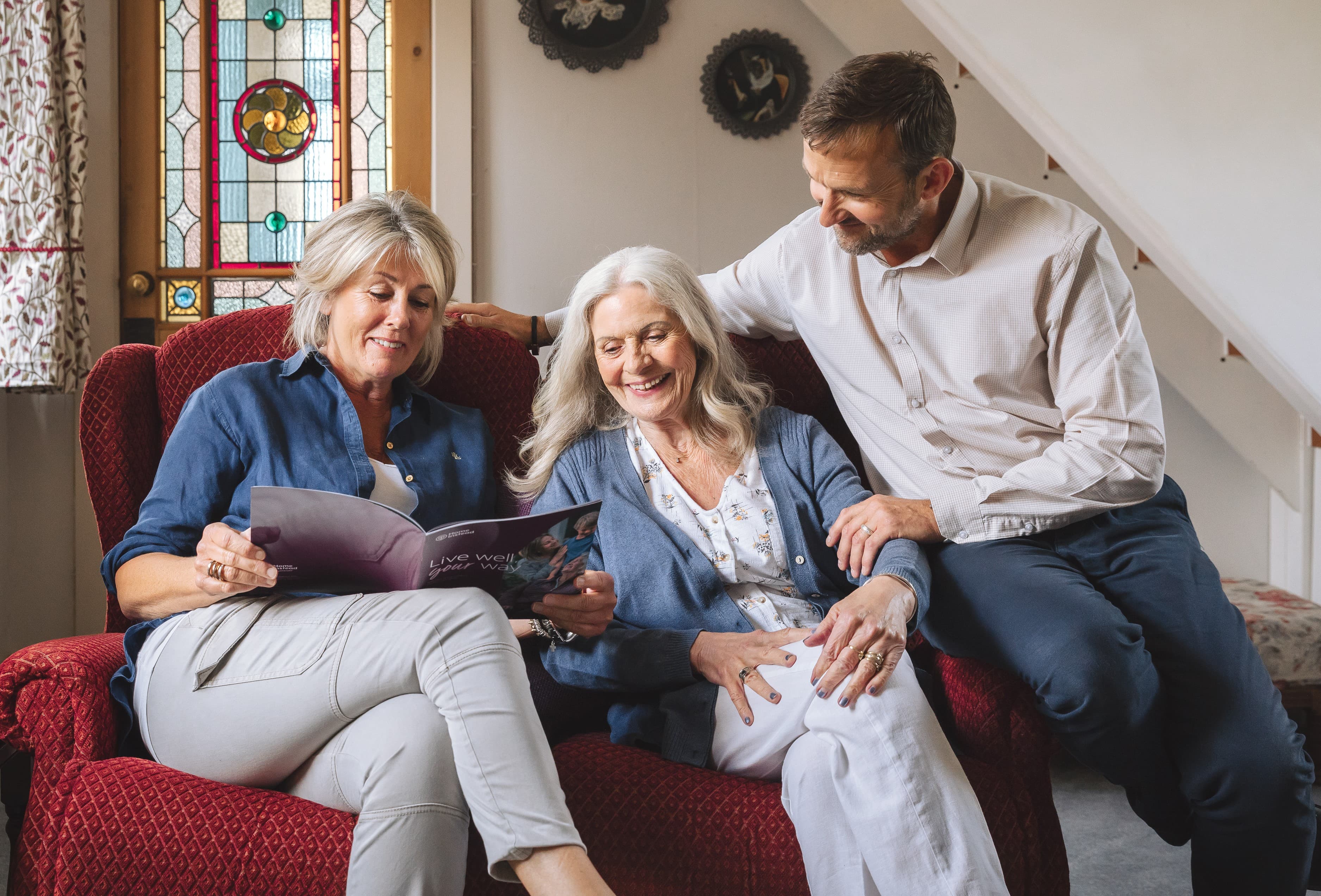 Elderly woman sitting on a sofa with a younger woman on one side and a younger man on the other, looking happy