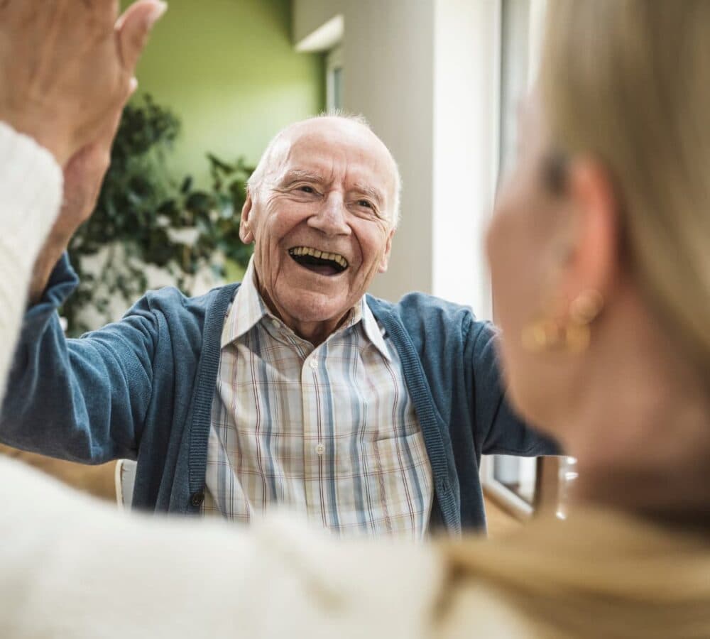 Smiling elderly man giving a high five to a woman in a bright, cheerful room. - Home Instead