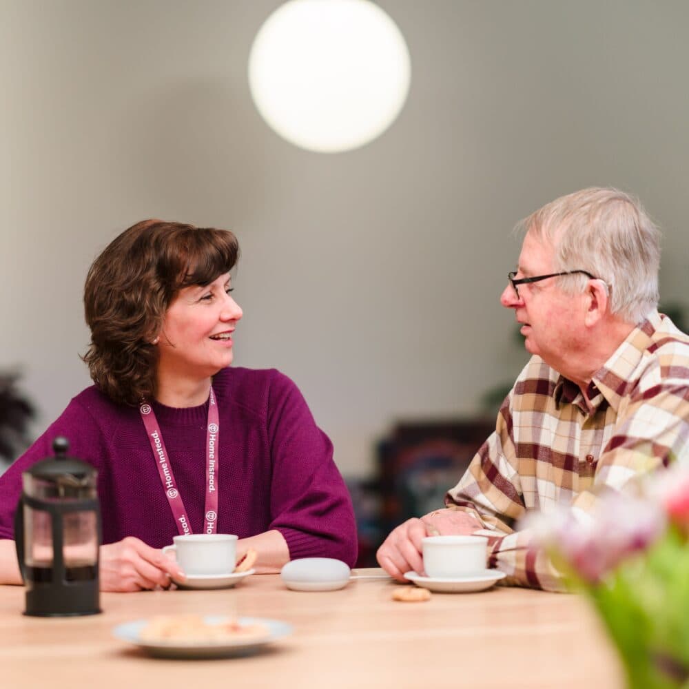 Male care client sitting drinking coffee and chatting with his female carer