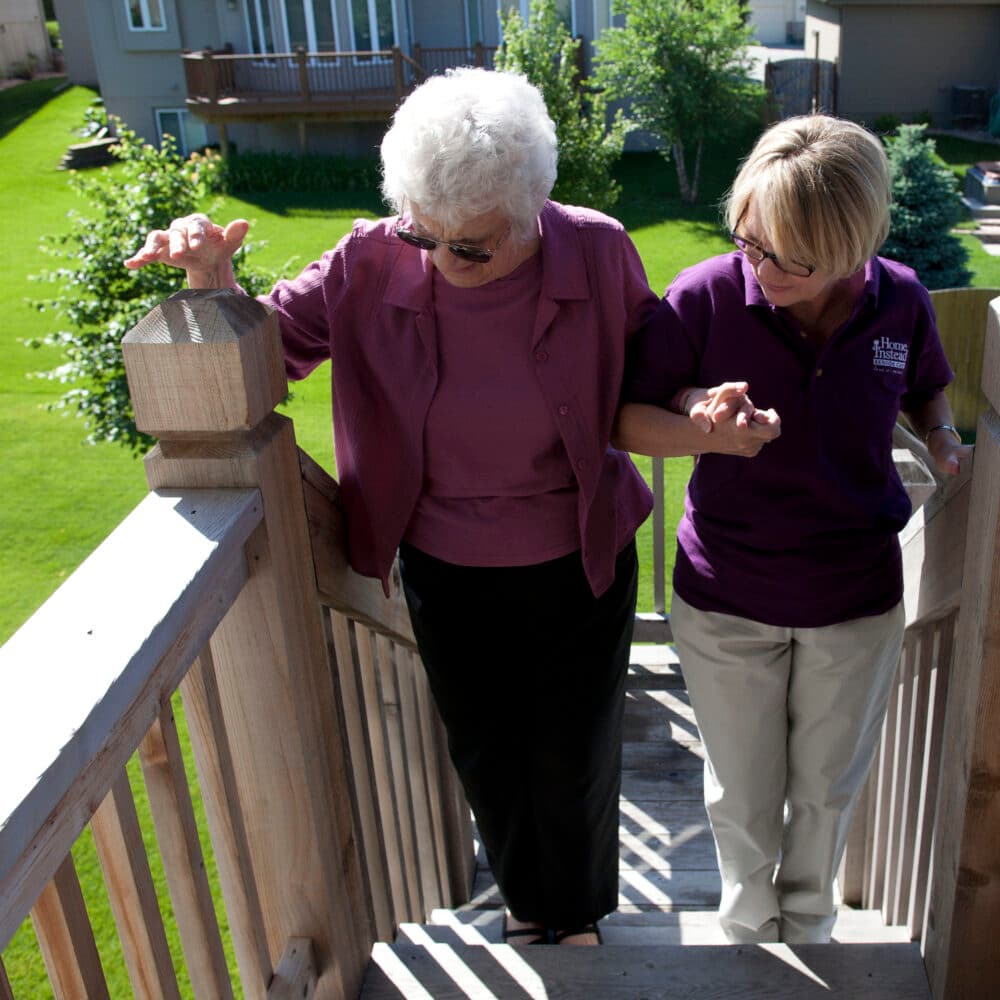 Female Home Instead carer helping her female client to climb an external wooden staircase