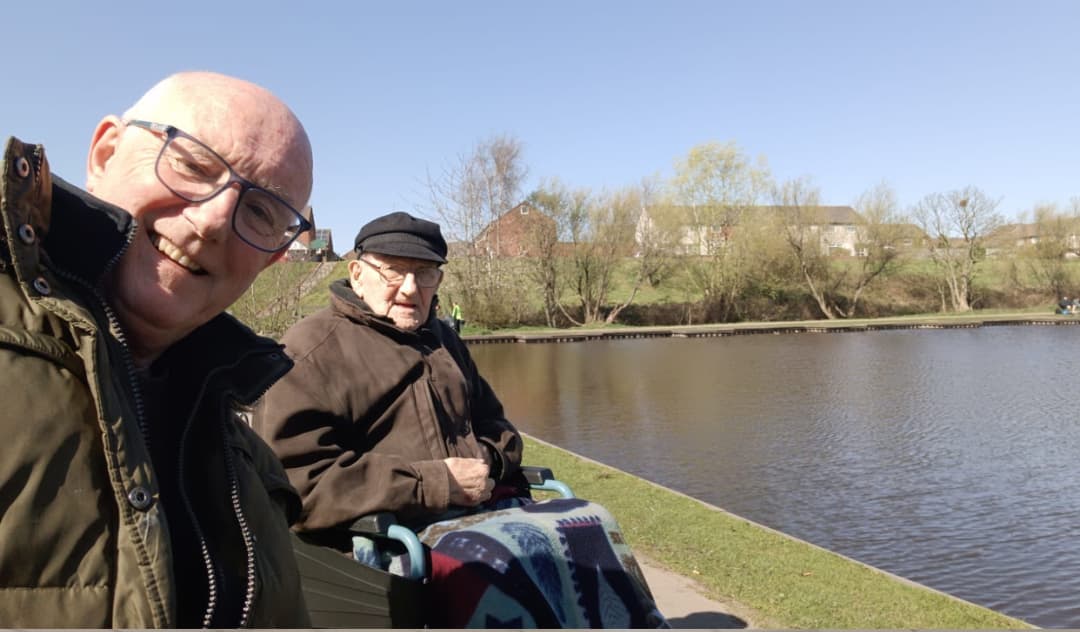 A man in a wheelchair by a river, then indoors at a fitness class with others. - Home Instead