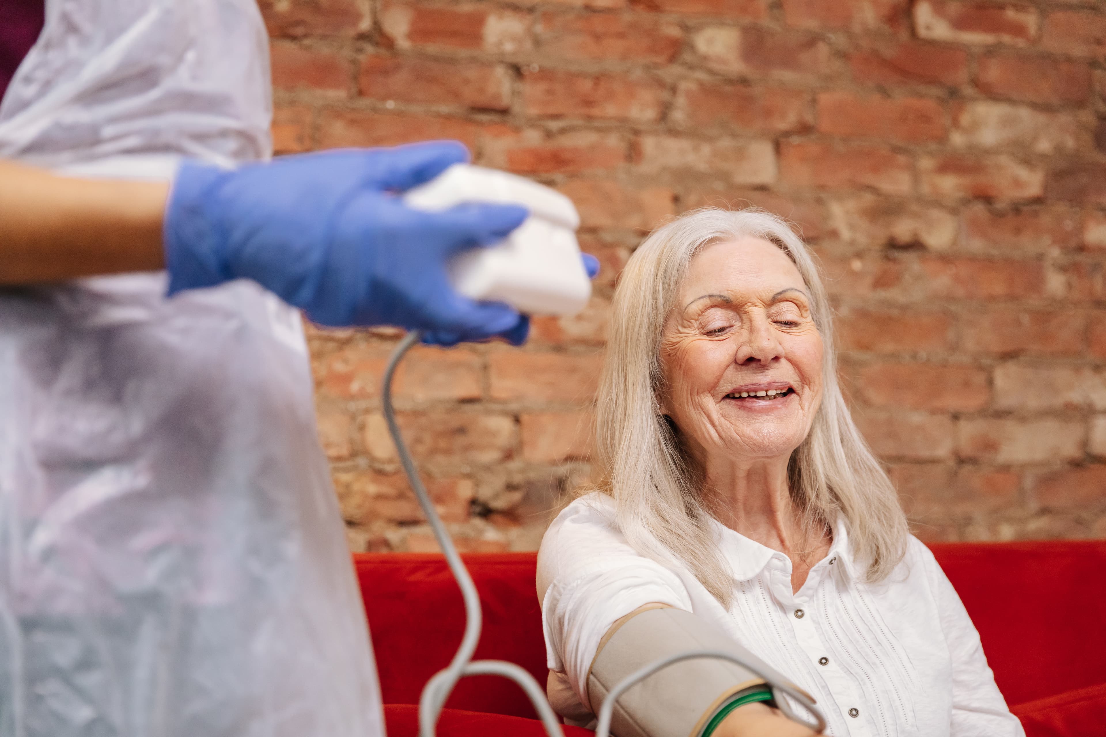 Smiling older woman gets her blood pressure checked by a healthcare worker wearing blue gloves. - Home Instead