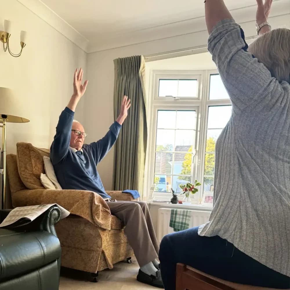 Home Instead client Don L. doing seated exercises with his live in care professional