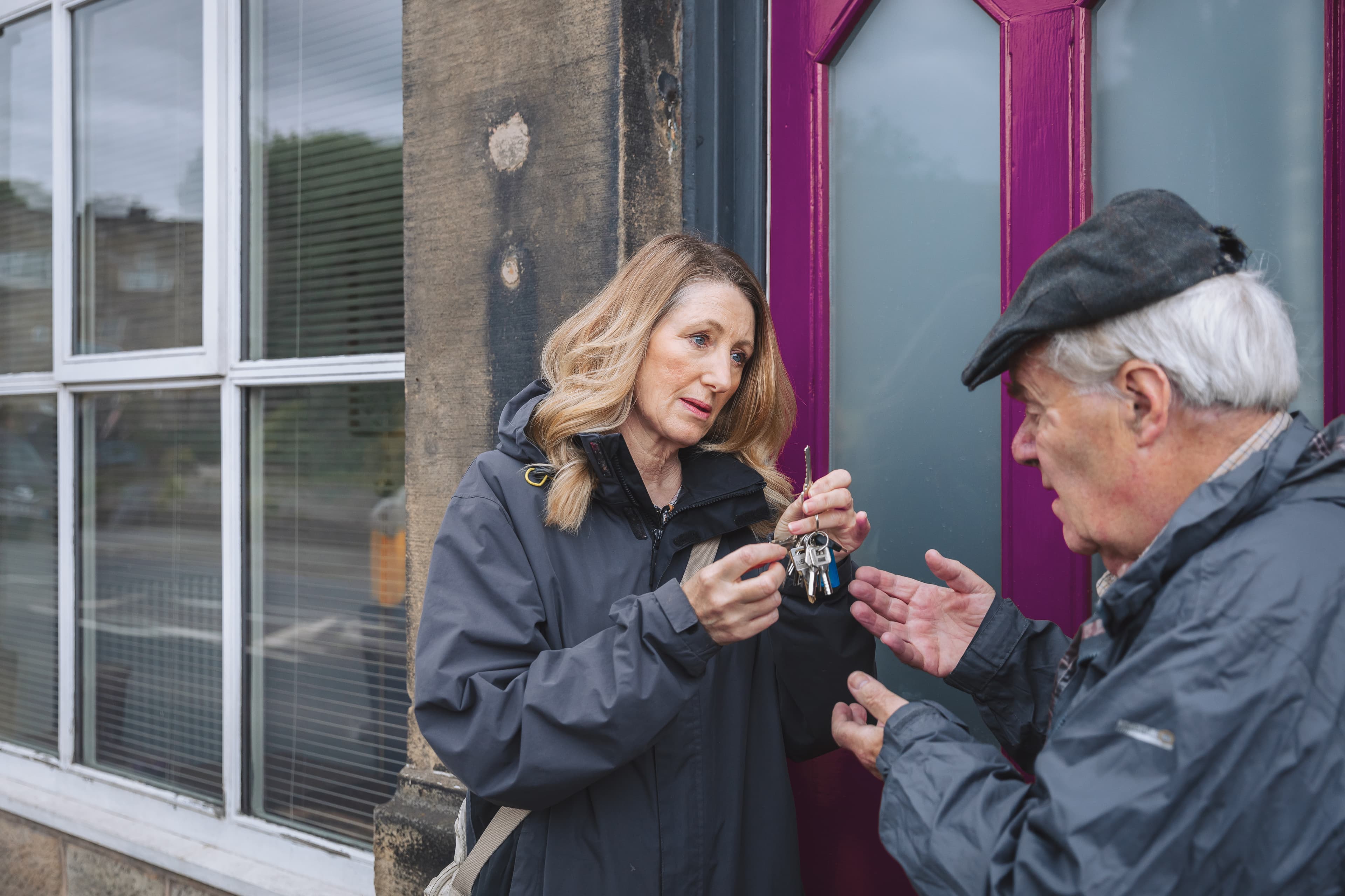 A woman hands a set of keys to an older man outside a building with a purple door. - Home Instead