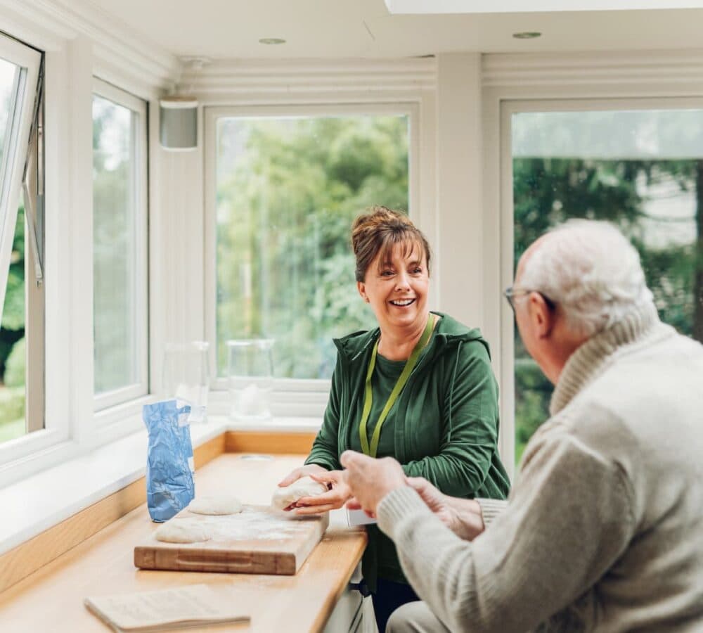 An older male adult with white haor chatting with his female carer inside the house
