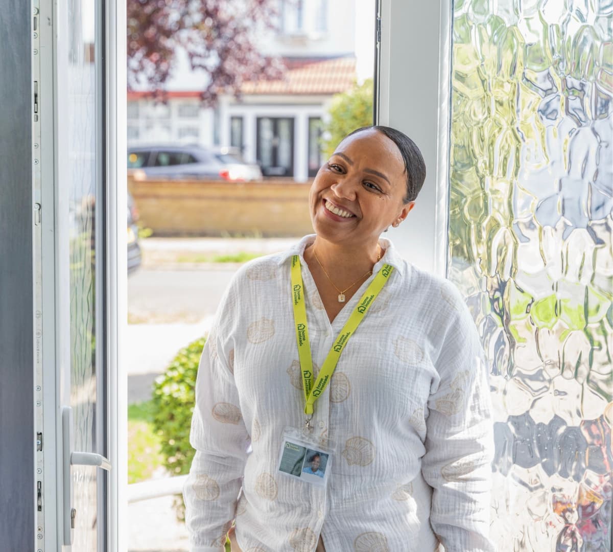A woman standing at the door with black hair and wearing long sleeves happy and smiling