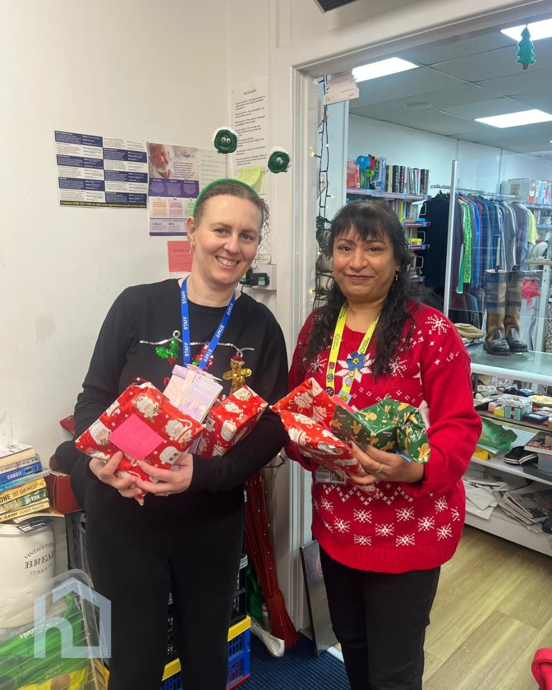 Two women smile while holding wrapped Christmas presents in a shop decorated for the holidays. - Home Instead