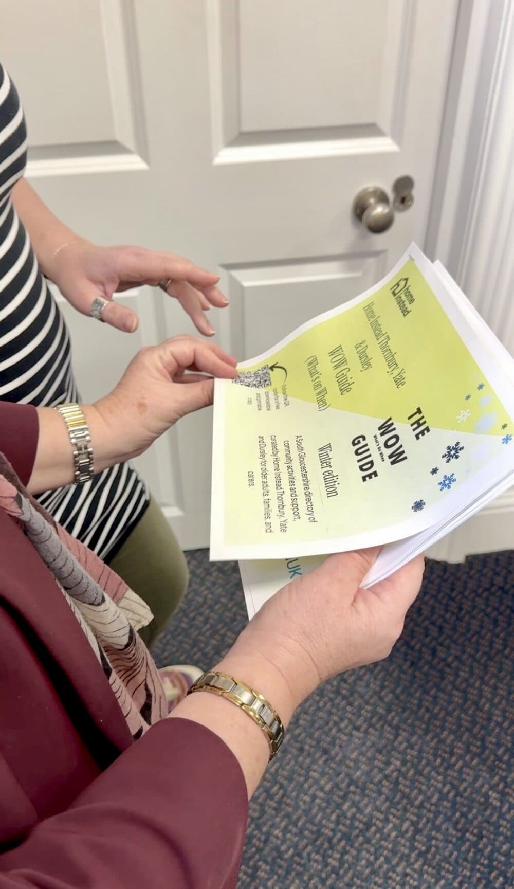 Two people holding and looking at a yellow booklet titled "THE WOW GUIDE" near a white door. - Home Instead