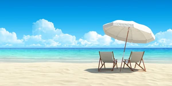 Two empty sun loungers under a white parasol on a sandy beach facing the sea and blue sky. - Home Instead