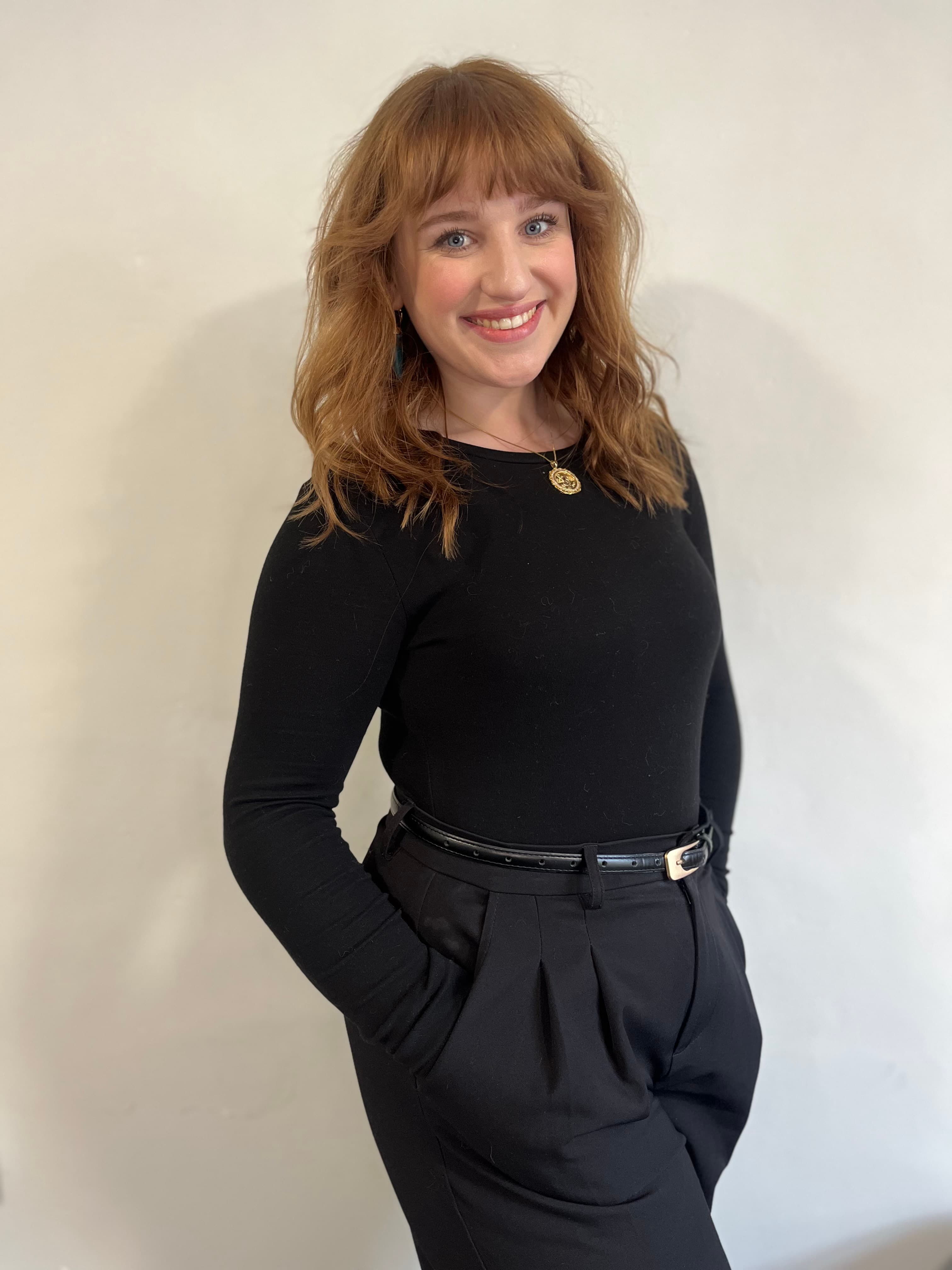 Woman with wavy red hair wearing a black long-sleeved top and black trousers, smiling at the camera. - Home Instead