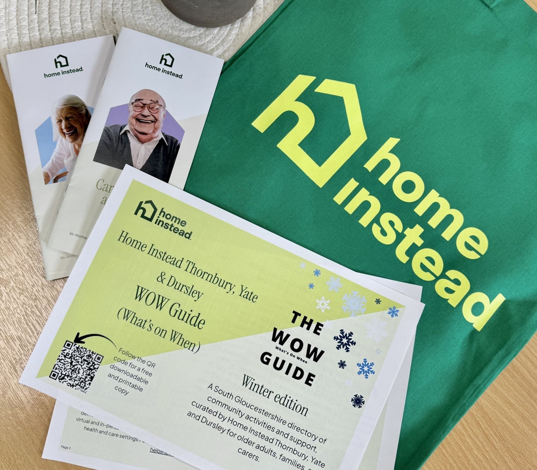Home Instead brochures, WOW Guide, and a green bag with the Home Instead logo displayed on a table. - Home Instead