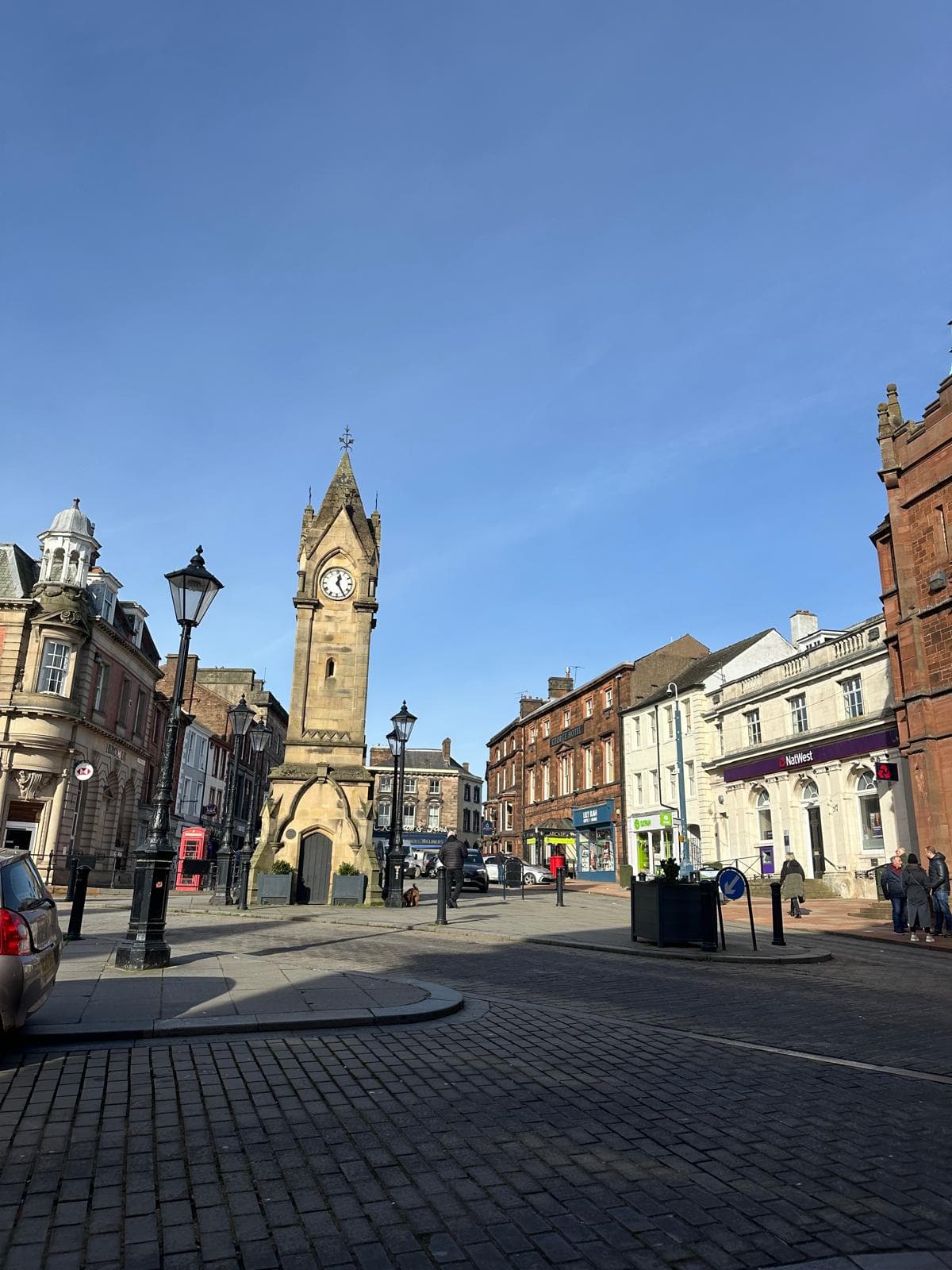 Town square with a tall clock tower, historic buildings, and a clear blue sky in the background. - Home Instead