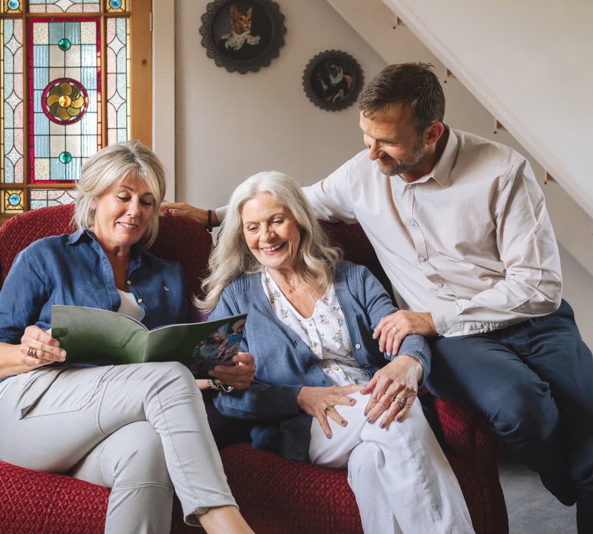 An older female adult with long white hair happy and smiling with her children chatting together while sitting on a couch