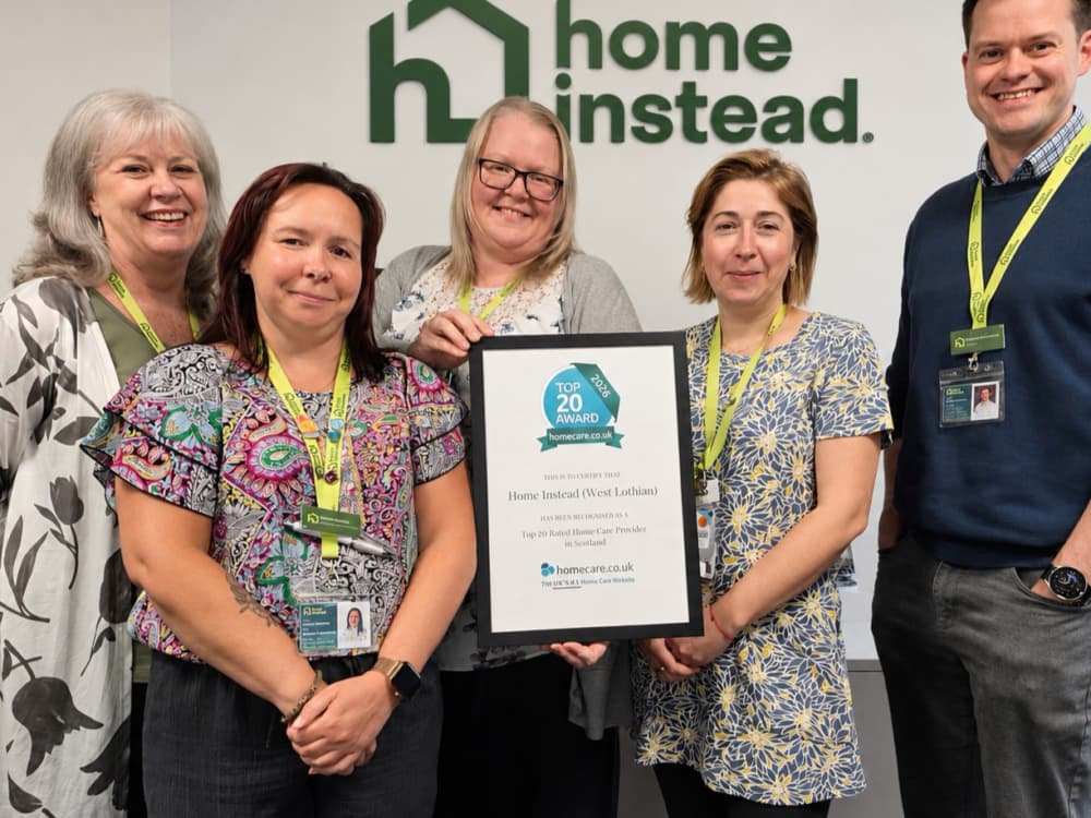 Five smiling people holding a framed award in front of a "Home Instead" logo on a wall. - Home Instead